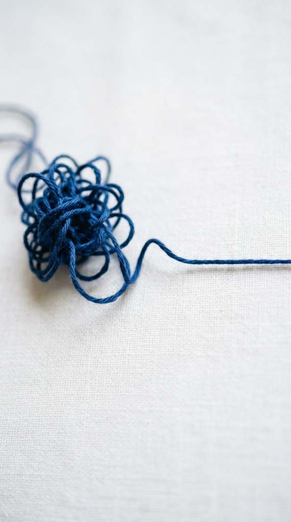 Blue thread untangling from a knot into a straight line on white linen