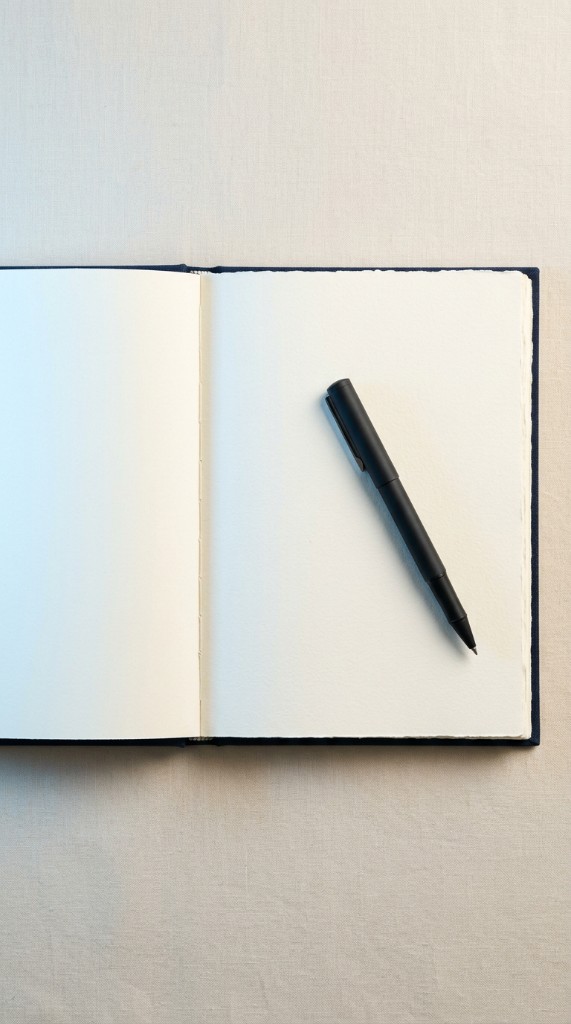 Open notebook with a blank page and pen resting across it in soft side light